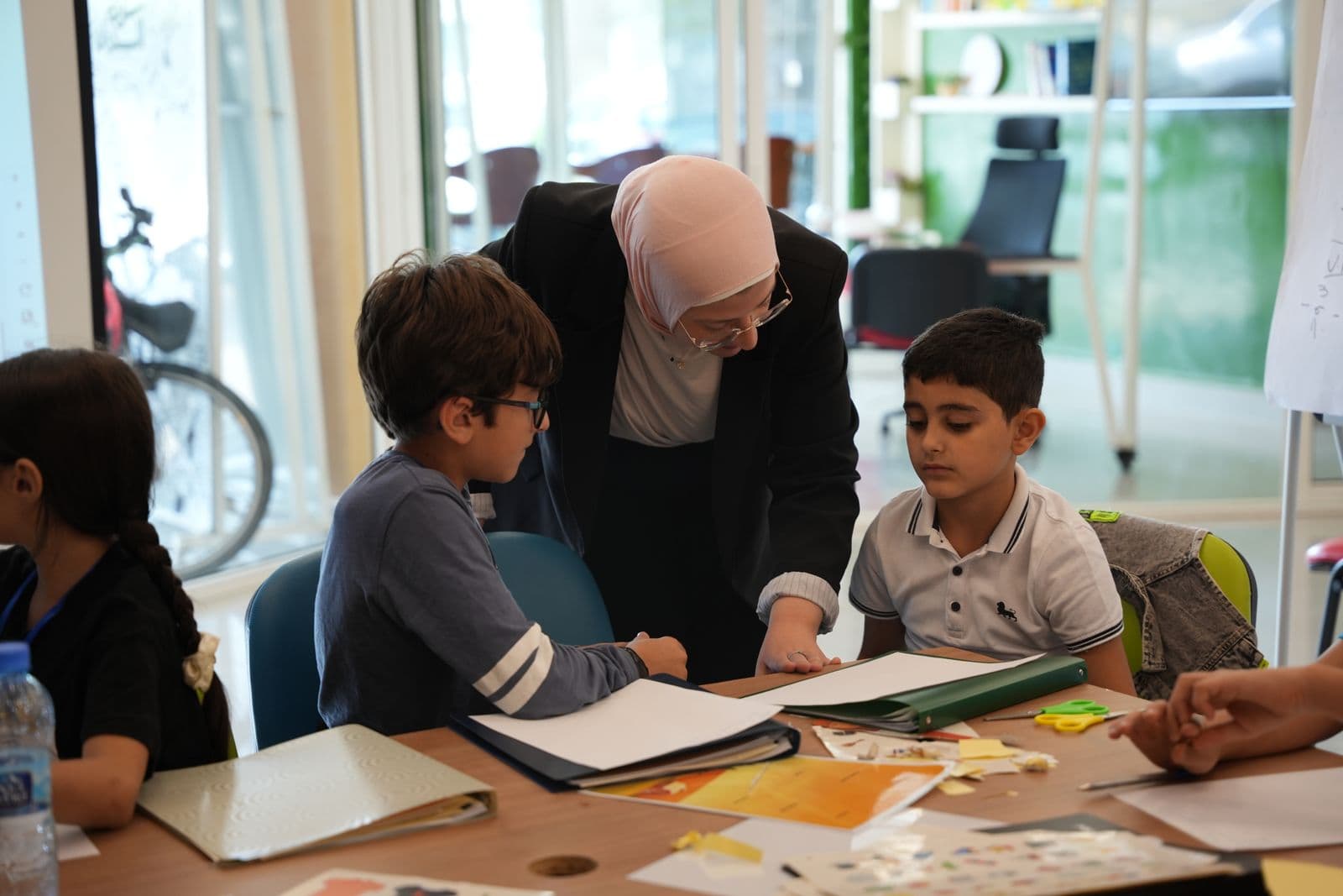 A facilitator leans in to guide two boys working on their worksheets at Youngpreneurs Academy