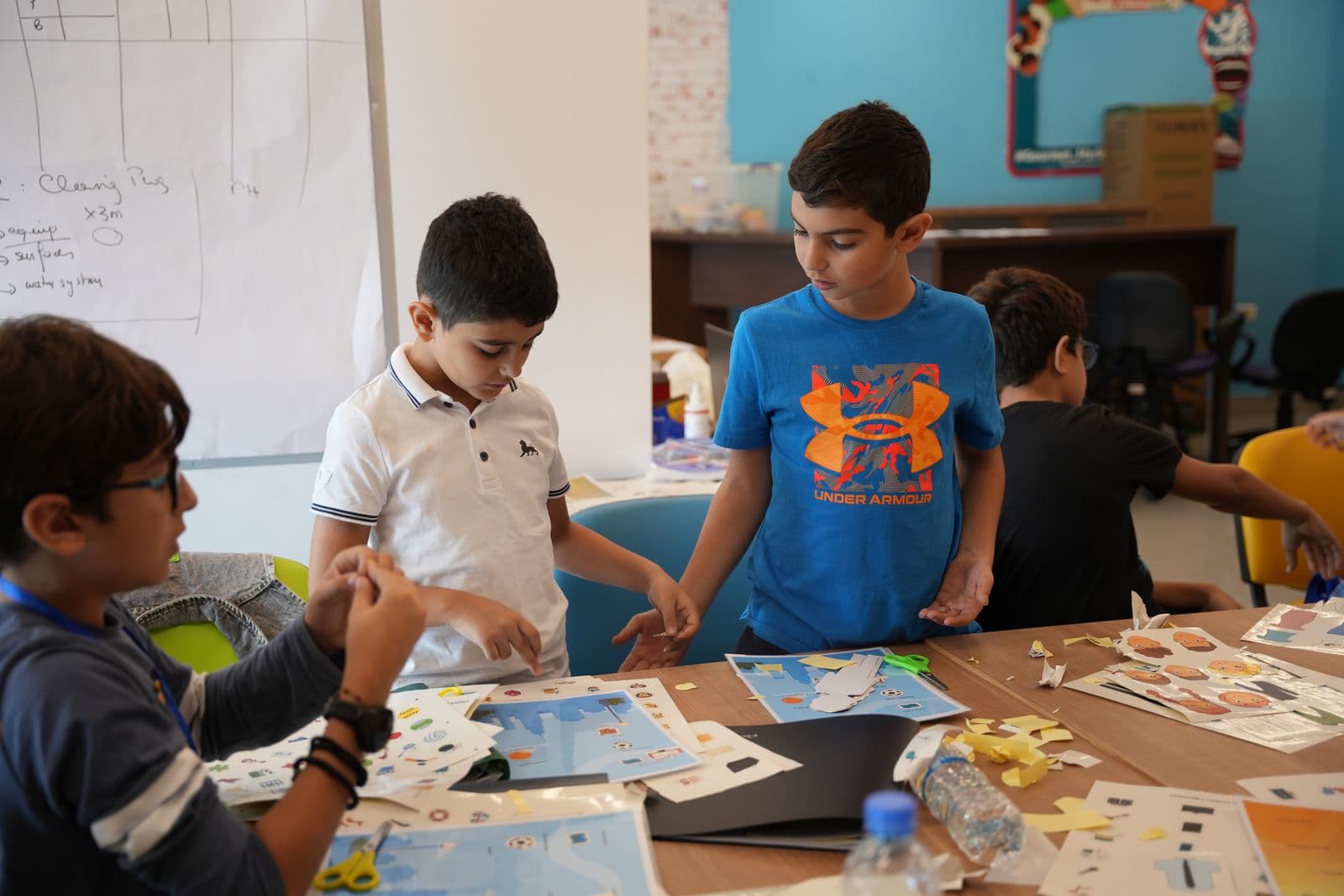 Young participants working together over worksheets and cut-outs at a shared table, Youngpreneurs Academy