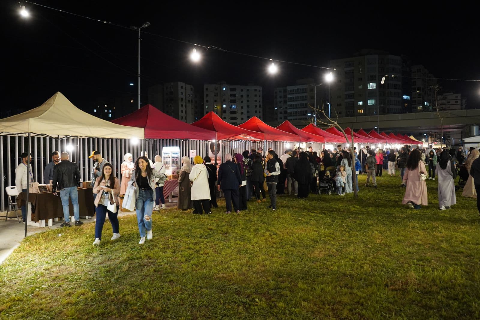 Visitors walking on the lawn between lit red and white stalls at the Gourmet Market in the evening