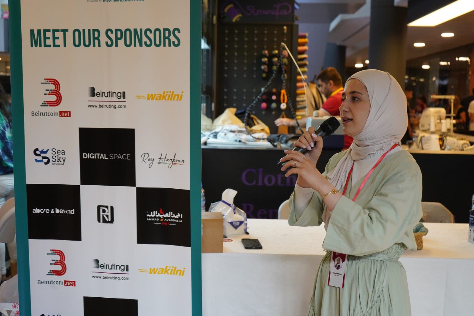 A speaker addresses the audience beside the sponsors wall at the Gourmet Market