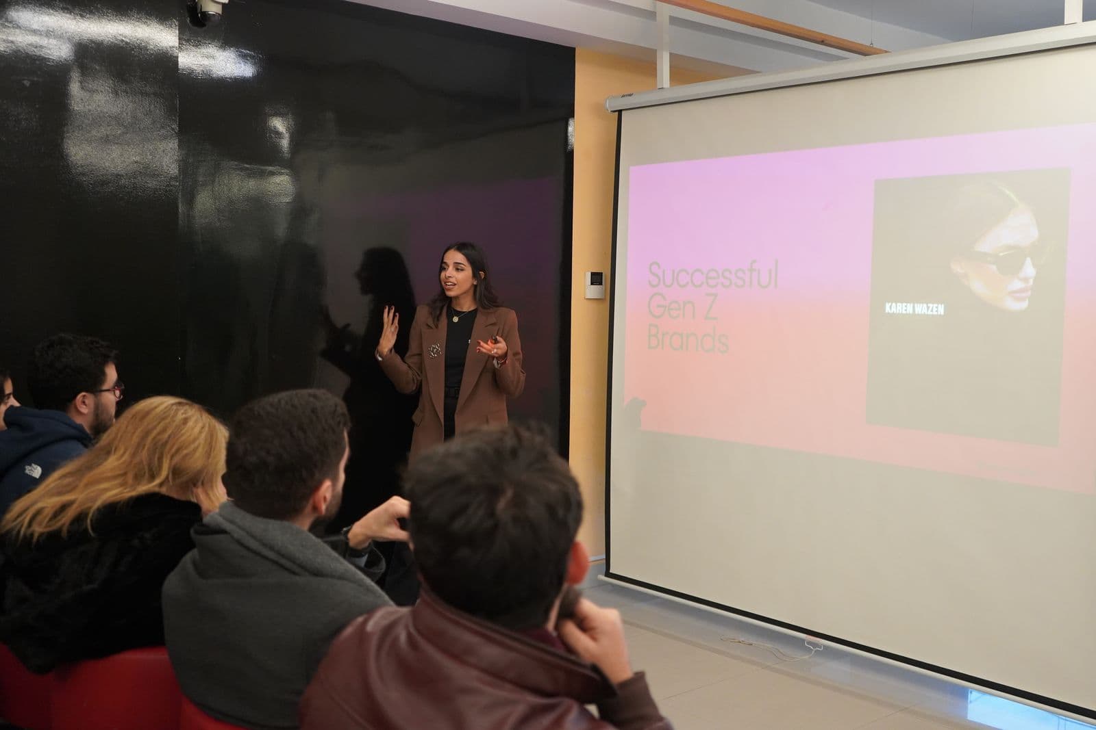 A speaker presents next to a projection screen while participants listen