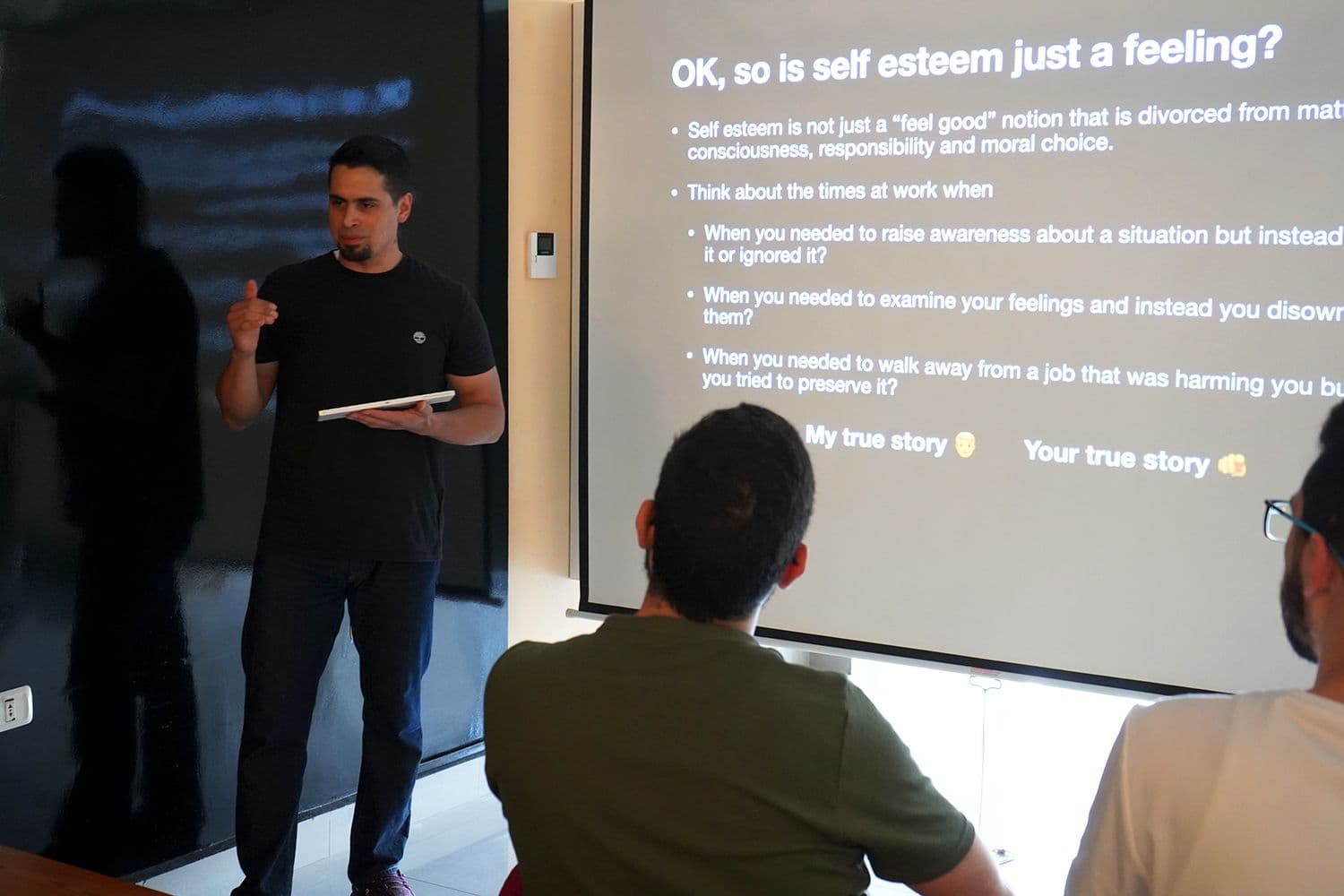 A trainer holding a tablet speaks beside a projected slide during a workshop