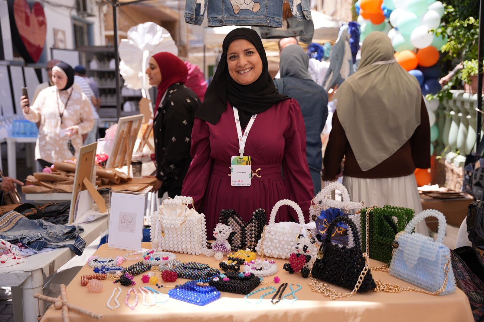 A woman stands behind her stall of handmade beaded bags at a Haretna market day