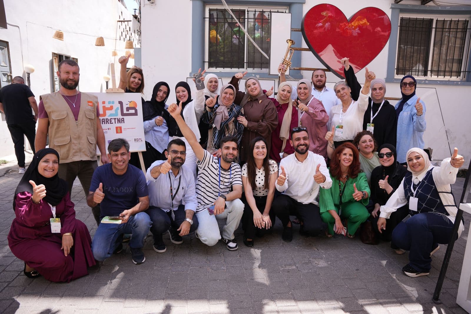 Participants and organisers gather for a cheerful group photo in the street under a Haretna sign