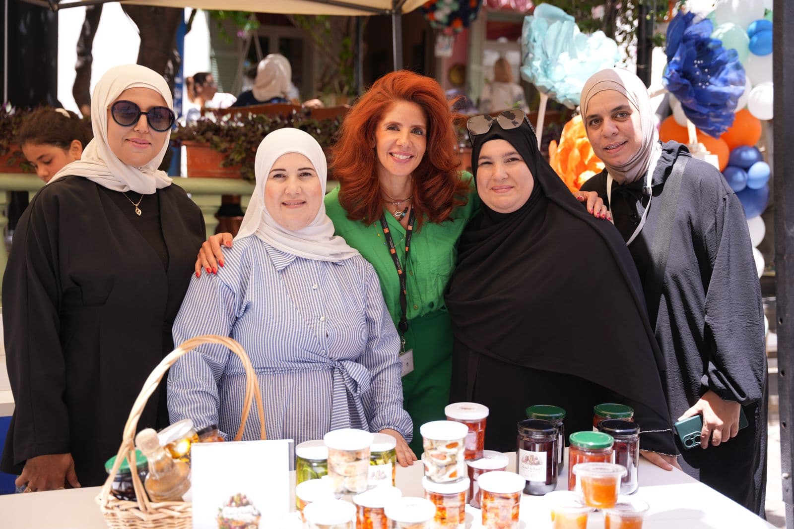 Four women pose together behind a table of jarred homemade food products at a Haretna market day