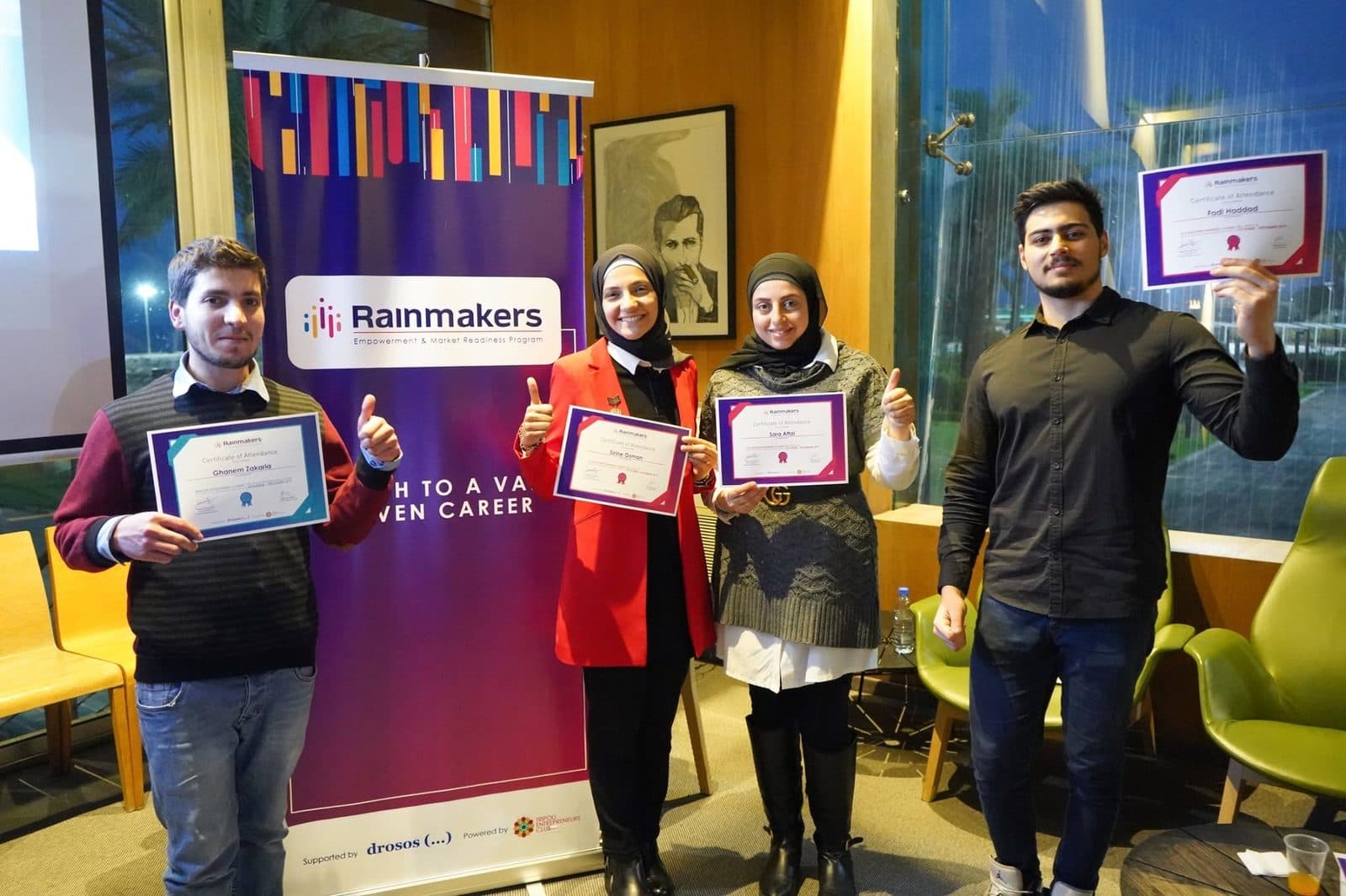 Graduates celebrate with their certificates beside the Rainmakers banner