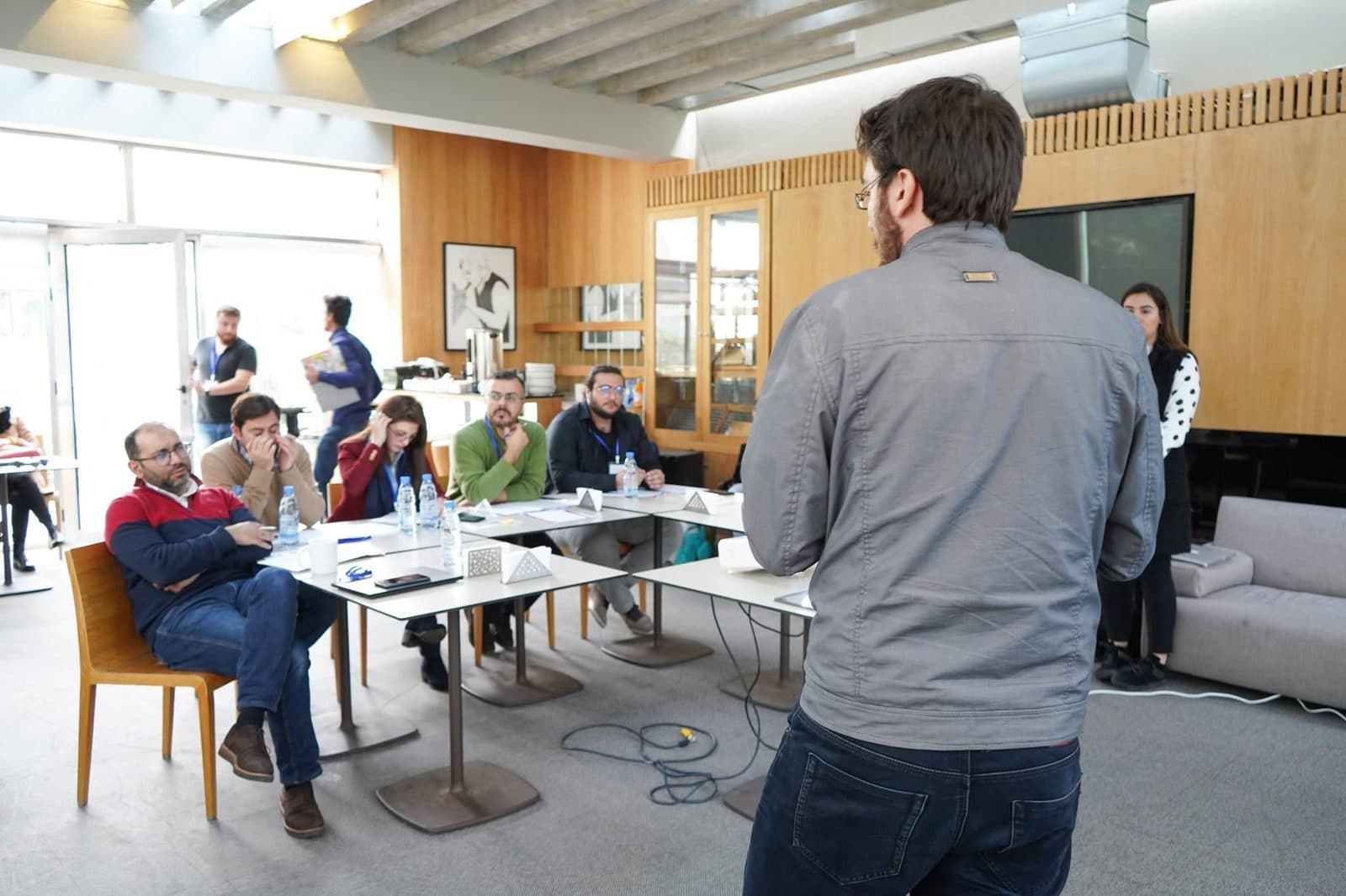 A trainer stands and addresses participants seated at tables
