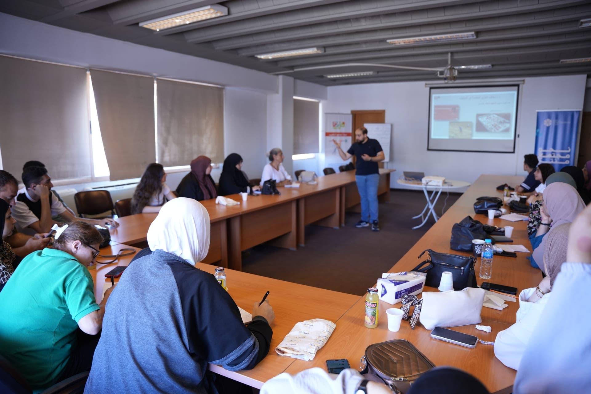 A trainer presents to women seated around conference tables during a Haretna training